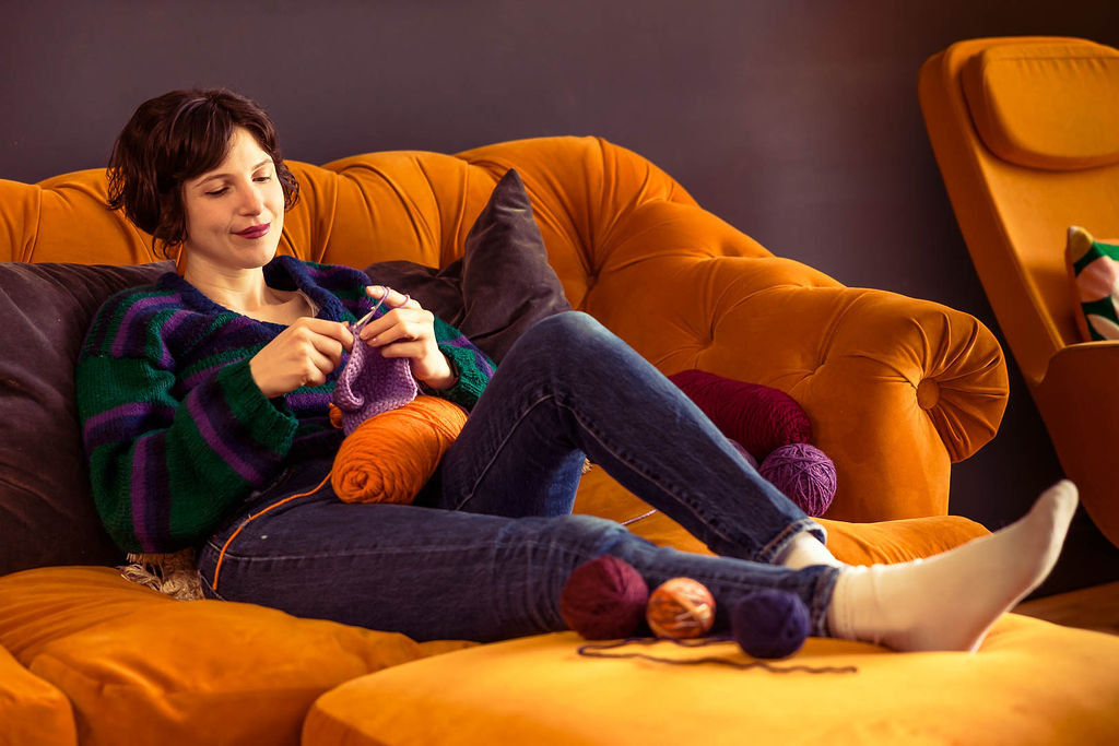 Maker crocheting on a sofa with yarn balls beside her